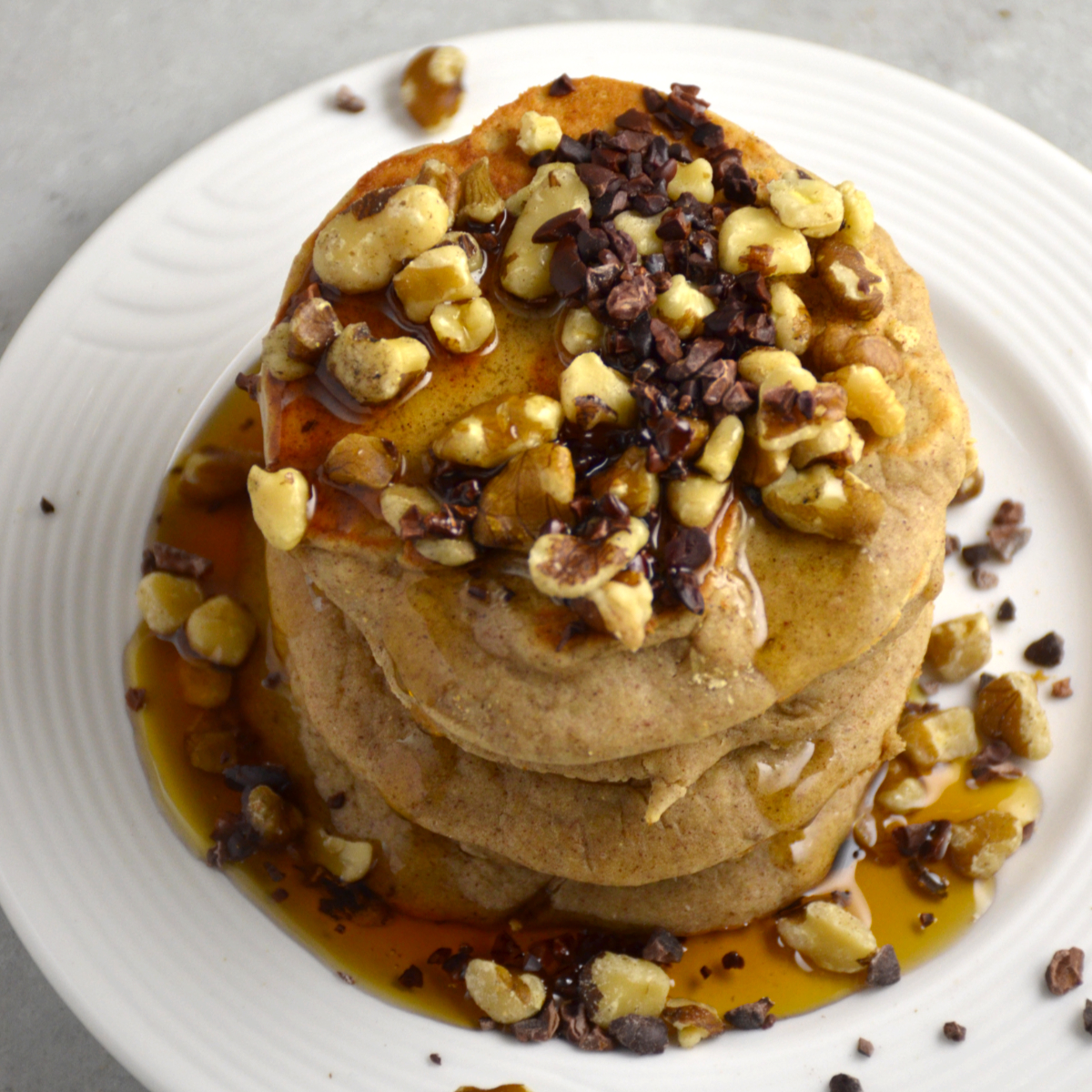 Gluten free, low FODMAP banana bread pancakes topped with walnuts, cacao nibs and syrup